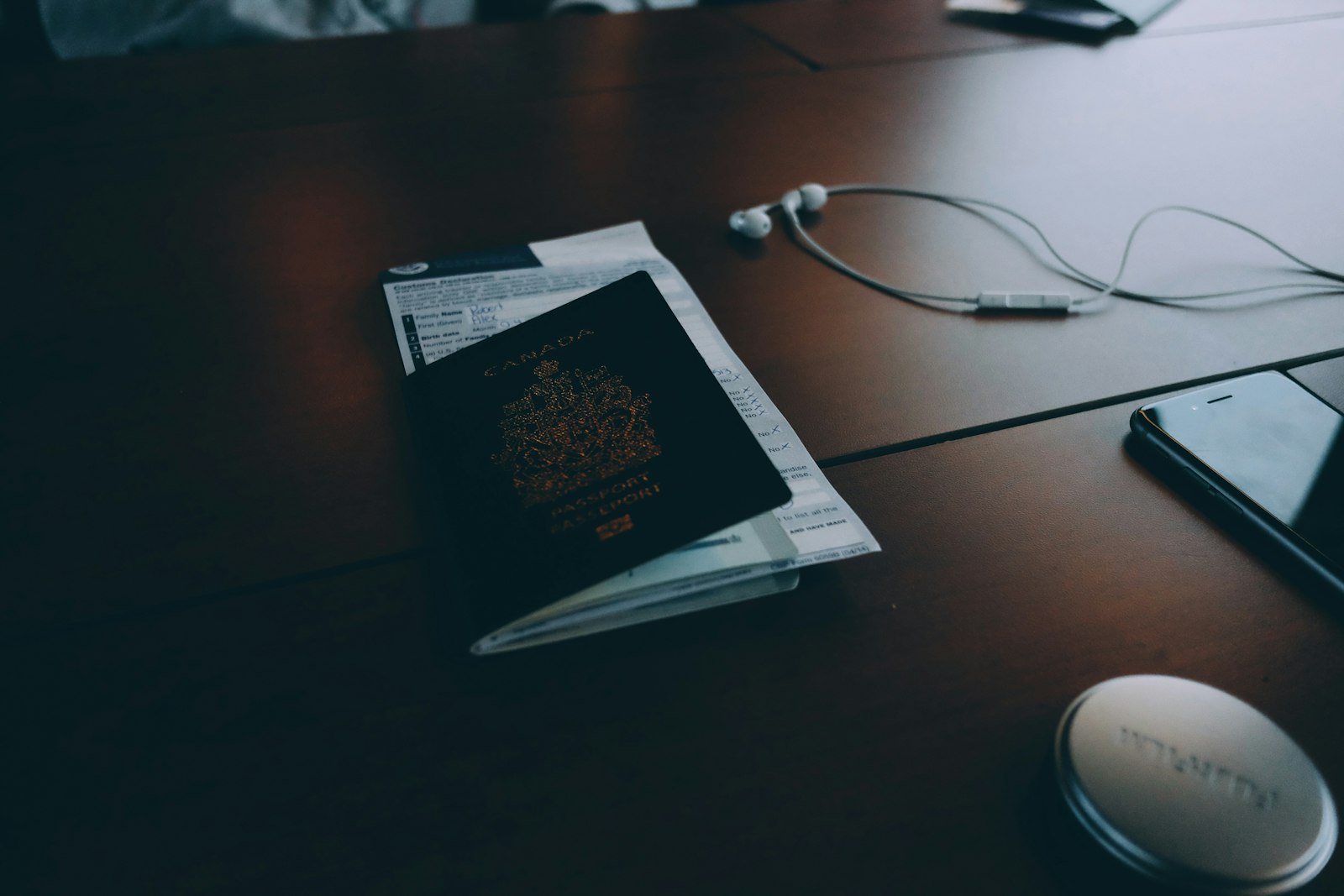 A Canadian passport resting on a customs declaration form on a desk, beside a phone and earphones