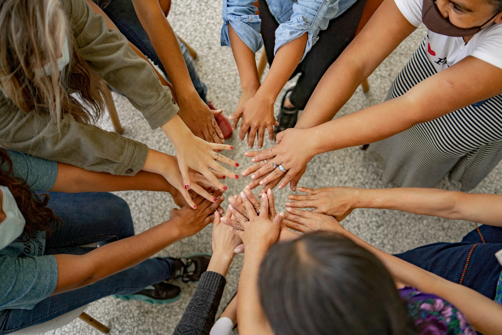 A diverse group of people reaching their hands together into the centre of a circle